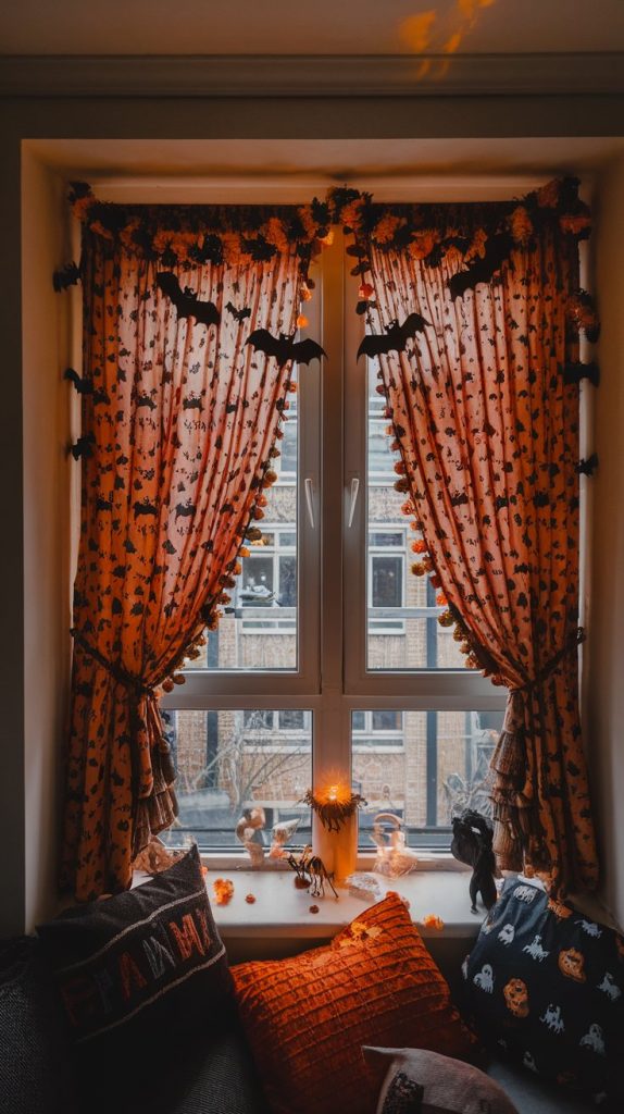 an apartment window nook with orange Halloween curtains, bat garland, flickering candlelight, spooky figurines